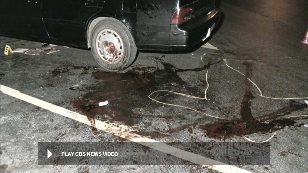 View showing most of the blood markings on the pavement. Video taken after the body was removed. Note the items under the vehicle. The severed belt buckle has already been secured at the time of this video. Still from CBS News video.