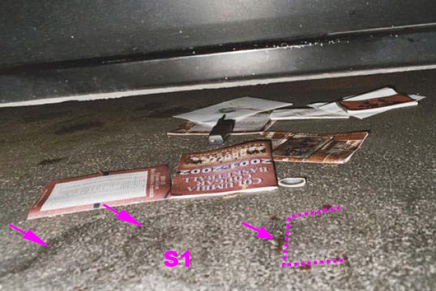 View of several magazine and other paper items found under the Heitholt Maxima. Heitholt’s cell phone and right lens of his glasses are also under the car. Note the several pavement scuff marks this side of magazines. These pavement scuff marks were denoted as site S1 in earlier photo. Two of the largest scuff marks are highlighted by the two arrows on the left. Also note blood drops in a near rectangular outline with several on top of the pavement scuff marks. The arrow in the middle of the rectangular outline points to what appears to be several drops in a line. This may also have been a laydown location for the assault weapon. Modified CBS News police photo from Internet.